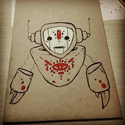 a robot with a white mask and red markings with pincers for hands drawing on cardboard